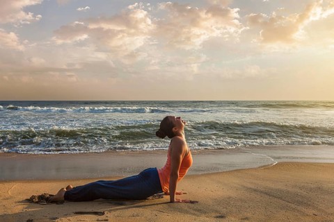 Yoga outdoors on beach, woman practices Ashtanga Vinyasa yoga Surya Namaskar Sun Salutation asana