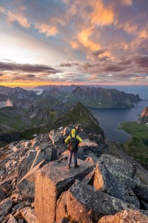 View over mountain top and sea, dramatic sunset, mountaineers at Hermannsdalstinden peak, with