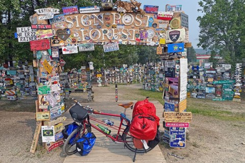 Bicycle with luggage in front of town and road signs in the signpost forest, cycling trip, cycling