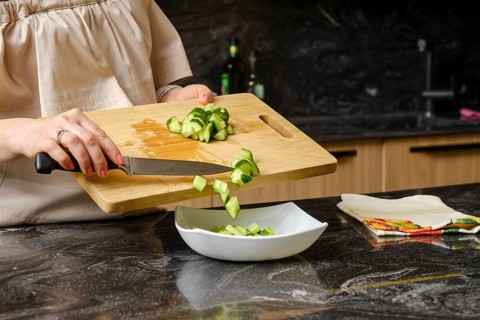 Closeup of hands of woman dropping a sliced cucumber into a dish with salad
