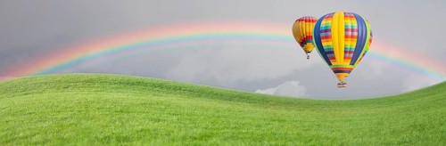 Hot air baloons drift above grass field with rainbow in the sky