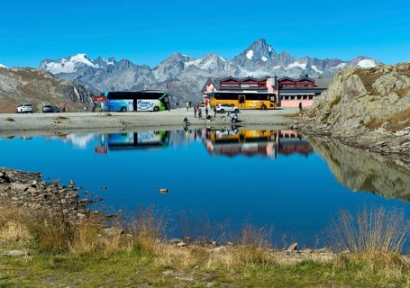 Coach with tourists and yellow bus of the Swiss PostBus AG on the Nufenen Pass, behind the mountain