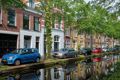Delft, Netherlands, May 12, 2017: Cars and bicycles parked on canal embankment in street of Delft