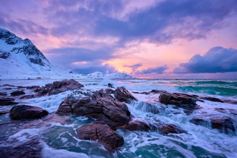 Waves of Norwegian sea on rocky coast in fjord on sunset with sun. Skagsanden beach, Lofoten