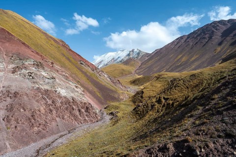 Valley with mountain stream between high mountains in autumn, mountain landscape with glaciated