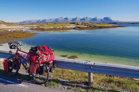 Packed touring bike, crystal clear water in a shallow bay, view of the mountain range Seven