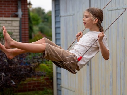 Boy swinging while sitting on children's swing at shed and garden gate, Germany, Europe