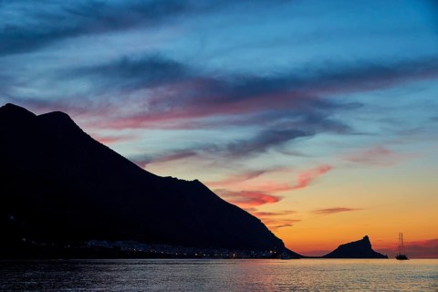 Blue evening sky, pink illuminated clouds, rocky coast, sunset, dusk, lanterns, sailboat,