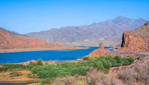 Blue Toktogul reservoir between dry mountain landscape with red mountains, Jalalabad region,