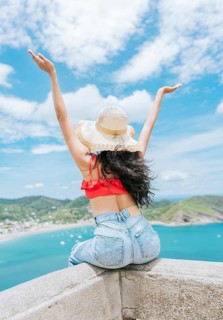 Lifestyle of woman on vacation sitting spreading hands to the beach. Tourist girl in hat spreading