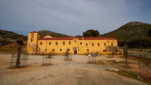 Fortress-like ochre building, façade, forecourt, enclosed trees, cloudy blue sky, Gouverneto,