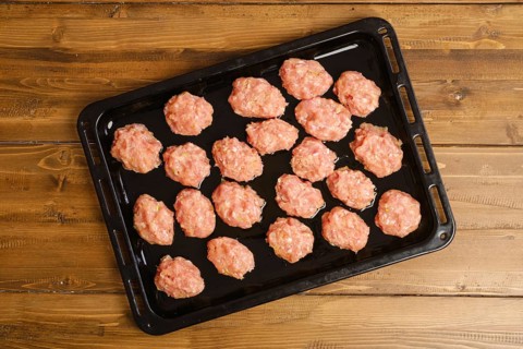 Top view of raw meatballs of minced meat on a baking tray on kitchen table