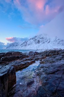 Beach of Norwegian sea on rocky coast in fjord on sunset in winter. Vareid beach, Lofoten islands,