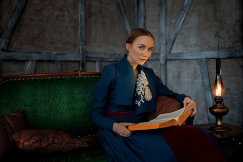 Attractive lady in oldfashioned clothes reading ancient book near vintage kerosene lamp
