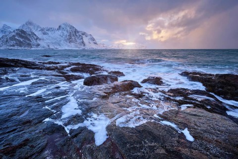 Beach of Norwegian sea on rocky coast in fjord on sunset in winter. Vareid beach, Lofoten islands,