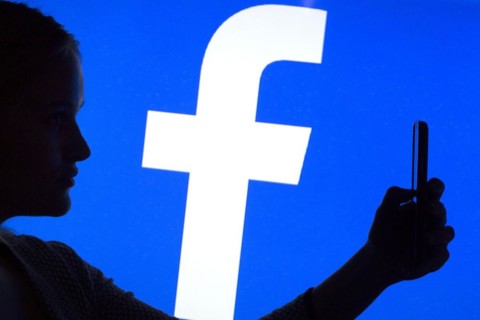 Silhouette of a woman with a smartphone in her hand in front of a Facebook logo, 12/01/2016