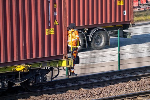 Shunter, railway employee steering the freight train with containers from the running board of the
