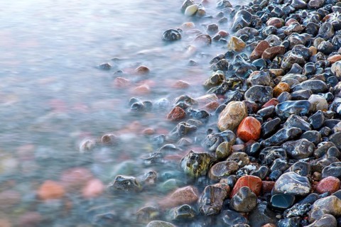Blurred sea water of wave rolling over wet colourful pebbles on shingle beach, cobble beach