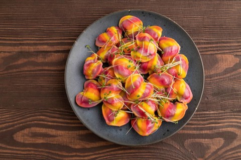 Rainbow colored dumplings with pepper, herbs, microgreen on brown wooden background. Top view, flat