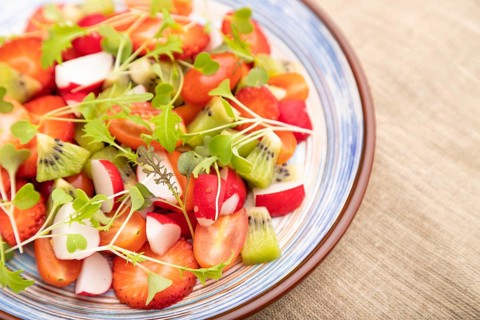Vegetarian fruits and vegetables salad of strawberry, kiwi, tomatoes, microgreen sprouts on black