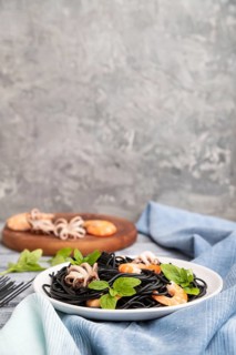 Black cuttlefish ink pasta with shrimps or prawns and small octopuses on gray wooden background and