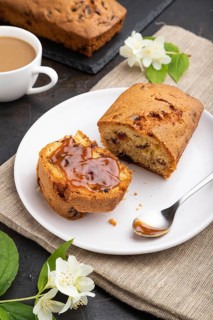 Homemade cake with raisins, almonds, soft caramel and a cup of coffee on a black concrete