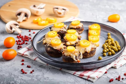 Stuffed fried champignons with cheese, kumquats and green peas on a gray concrete background.