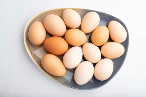 Pile of colored chicken eggs on plate isolated on white background. top view, flat lay, close up