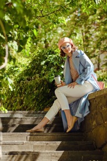 Hipster woman sitting at an outdoor stone bench, enjoying tea and sunshine