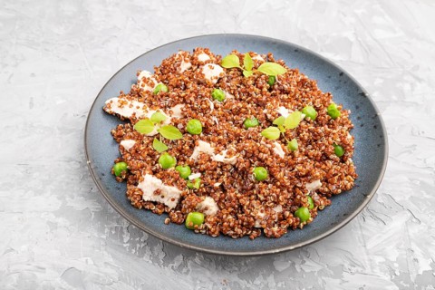 Quinoa porridge with green pea and chicken on ceramic plate on a gray concrete background. Side