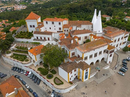 Overview of a historic castle with white towers and orange-red roofs, surrounded by a city, aerial