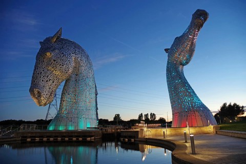 The Kelpies, two monumental horse sculptures, glow in bright colours at night, Forth and Clyde