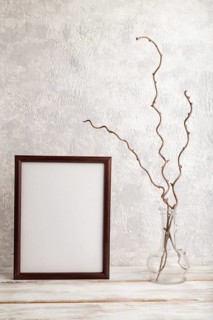 Brown wooden frame mockup with dried wine branch in glass on gray concrete background. Blank,