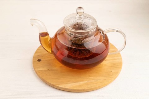 Red tea with herbs in glass teapot on white wooden background. Healthy drink concept. Top view,