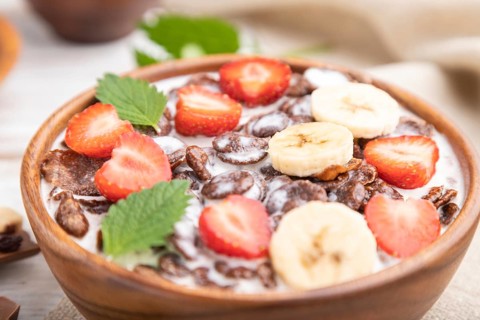 Chocolate cornflakes with milk and strawberry in wooden bowl on white wooden background and linen