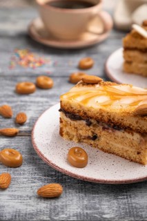 Honey cake with milk cream, caramel, almonds and a cup of coffee on a gray wooden background and