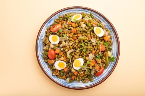 Mung bean porridge with quail eggs, tomatoes and microgreen sprouts on a pastel orange background.
