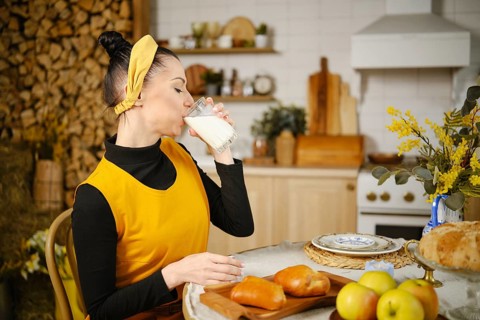 Woman drinking milk while sitting at the table in rustic style kitchen. The table is served with