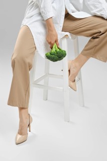 Daily healthy eating concept. Cropped image of woman sitting on chair with broccoli in hand
