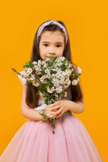 Cute young girl with bouquet of spring flowers over yellow background