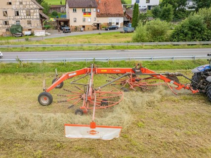 Close-up of a haymaking machine in a field, with a building and a road in the background, Dachtel.