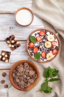 Chocolate cornflakes with milk and strawberry in wooden bowl on white wooden background and linen