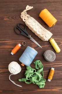 Sewing accessories: scissors, thread, thimbles, braid on brown wooden background. Top view, flat