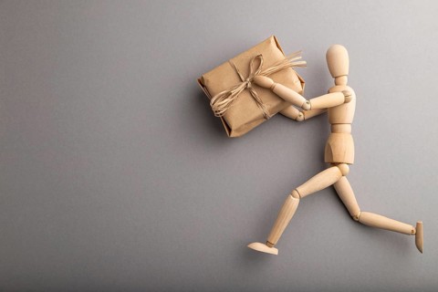 Wooden mannequin holding a gift box on gray pastel background. copy space, isolated, delivery