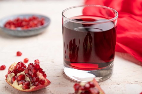 Glass of pomegranate juice on a white concrete background with red textile. Side view, close up,