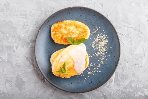Cheese pancakes on a blue ceramic plate with milk sauce on a gray concrete background. top view,