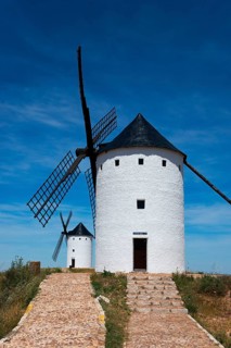 Two white windmills stand under a clear blue sky, embedded in a natural summer landscape, Alcazar