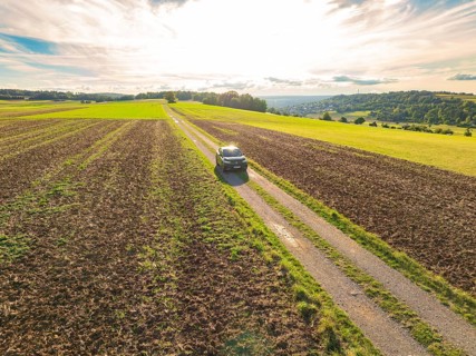 A car drives along a rural road, surrounded by expansive fields under bright daylight, car sharing,