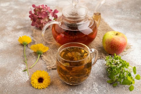 Red tea with herbs in glass teapot on brown concrete background and linen textile. Healthy drink