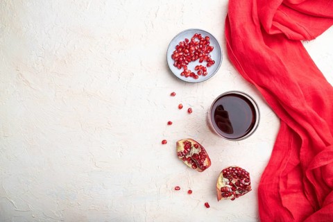 Glass of pomegranate juice on a white concrete background with red textile. Top view, copy space,